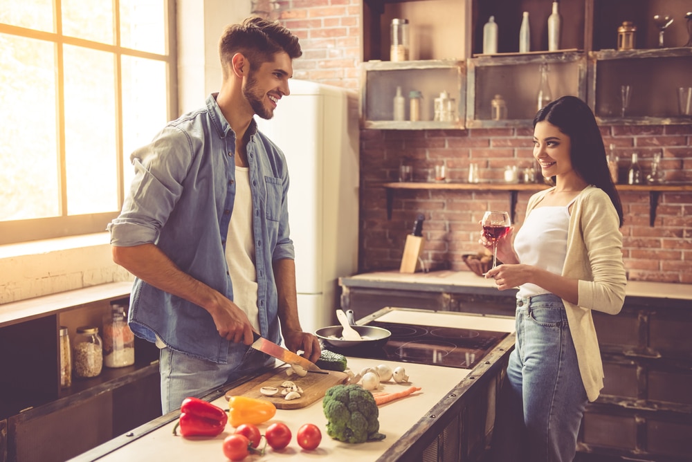 Man preparing dinner while woman watches on smiling